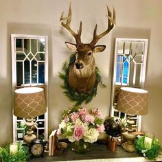 a deer head mounted to the wall above a mantle with flowers and candles on it