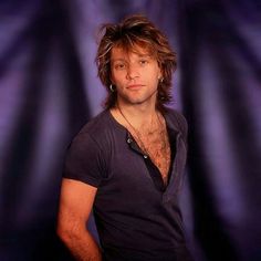 a man with long hair standing in front of a purple background