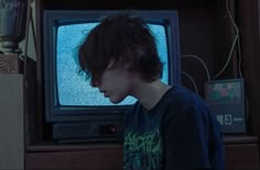 a boy is staring at an old tv in front of him with his head turned to the side