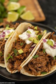 three pulled pork tacos with sour cream and avocado on a black plate