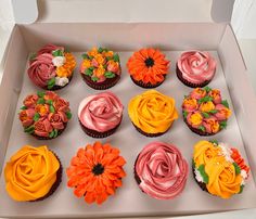 a box filled with cupcakes covered in pink and orange frosting flowers on top of each one