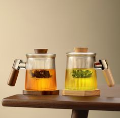 two glass teapots filled with green tea on top of a wooden table next to each other