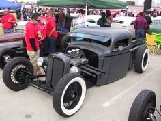 two men standing next to an old fashioned car at a car show in the parking lot