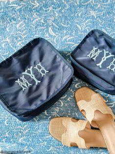 two pairs of shoes sitting on top of a bed next to a blue case with monogrammed letters