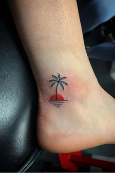 a small palm tree tattoo on the left side of the foot, with an orange sunset behind it