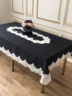 a black table with white doily and flowers in a vase on it, sitting on a wooden floor