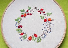 a cross - stitch wreath with cherries and leaves is displayed on a green cloth