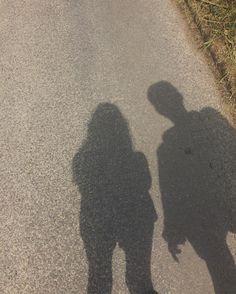 the shadow of two people standing next to each other on a street with grass in the background