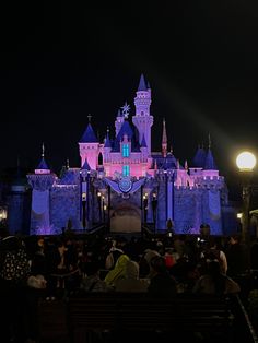 the castle is lit up at night with people sitting on benches in front of it