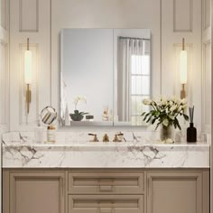 an elegant bathroom with marble counter tops and gold trim around the vanity, along with two vases filled with flowers