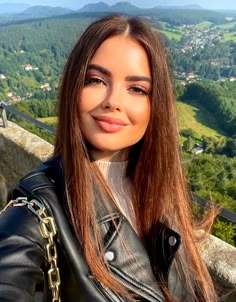 a woman with long hair wearing a black leather jacket and posing for a photo on top of a hill