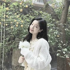 a woman standing in front of a tree holding flowers