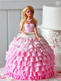 a barbie doll sitting on top of a pink dress next to a white wedding cake