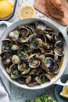 clams and lemons in a white bowl on a table next to sliced bread