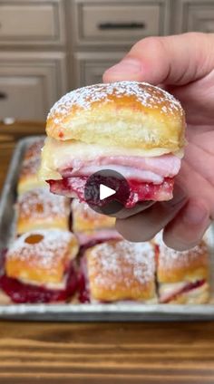 someone is holding up a sandwich in front of some pastries on a baking sheet