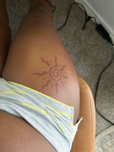 a woman with a sun tattoo on her lower back and leg, sitting in a chair