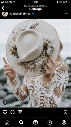 a woman wearing a white hat with flowers on the brim and holding her hands up in front of her face