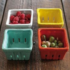 four plastic containers with raspberries and grapes in them on a wooden table top