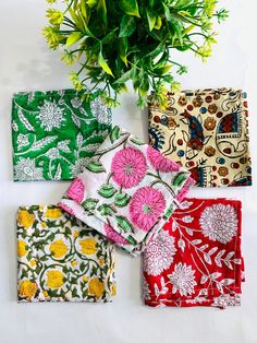 four napkins with flowers on them sitting next to a potted plant