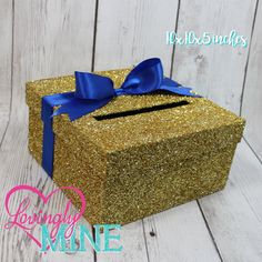 a gold glitter box with a blue bow on the top, sitting on a wooden surface