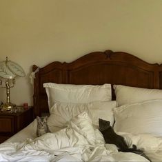 two cats sitting on top of a bed with white sheets and pillows, next to an alarm clock