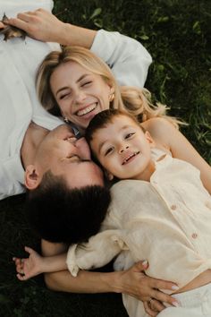 a man and woman laying on the grass with their child in front of them smiling