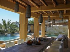 an outdoor dining area next to a swimming pool with wicker hanging from the ceiling