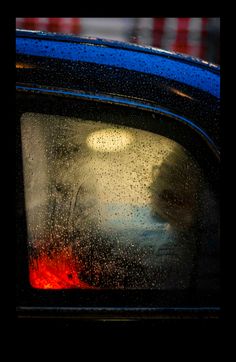 the back window of a blue car with rain drops on it's side mirror