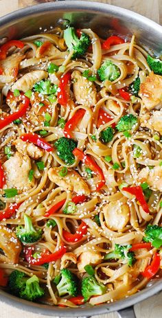 a skillet filled with noodles, broccoli and red peppers on top of a wooden table