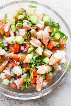 a glass bowl filled with shrimp, cucumber and tomato salad on top of a white table