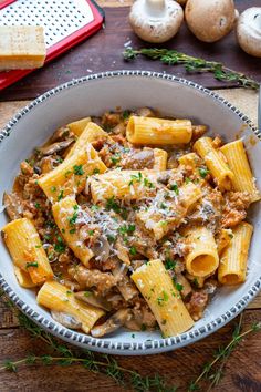 a bowl filled with pasta and mushrooms on top of a wooden table next to garlic