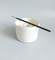 a white cup with a black handle and two holes on the rim, holding a pencil