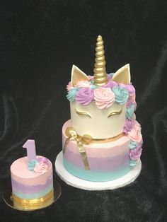 a birthday cake decorated with pastel pink, blue and gold icing has a unicorn horn on top