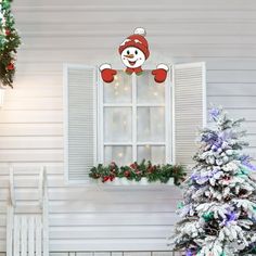 a christmas tree in front of a white house with snow on the windowsills