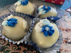 three white chocolates with blue flowers on them sitting on a plate next to a red box