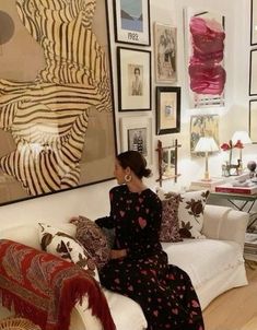 a woman sitting on top of a white couch in front of a wall covered with pictures