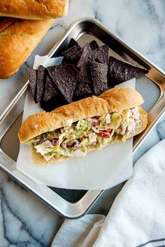 a tray with a sandwich and chips on it next to a baguette roll