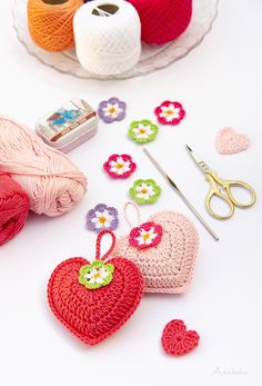 crocheted hearts, yarn and scissors on a white table with other crafting supplies