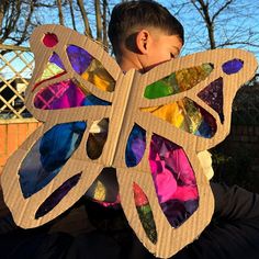 a young boy wearing a butterfly shaped cardboard cutout with colorful stained glass pieces on it's wings