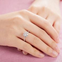 a woman's hand with a diamond ring on her left hand and a pink background