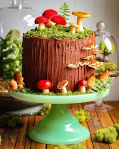 a chocolate cake with mushrooms and trees on top is sitting on a green pedestal, surrounded by moss