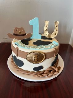 a birthday cake with a cowboy hat and number one on it, sitting on a wooden table