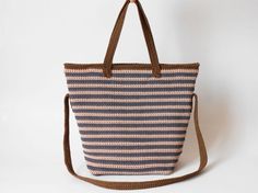 a blue and white striped tote bag on a brown leather strap, with the handles down