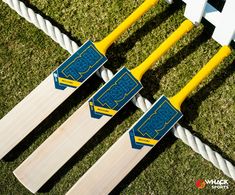 three wooden cricket bats sitting on top of green grass next to yellow and white poles