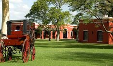 a horse drawn carriage on the grass in front of a red brick building with trees