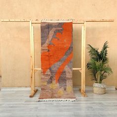 an orange and grey rug sitting on top of a wooden stand next to a potted plant