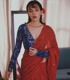 a woman in a red and blue sari with jewelry on her neck standing next to a mirror