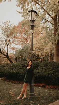 a woman leaning against a lamp post in the grass