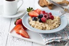 a bowl of oatmeal with berries and strawberries next to a cup of coffee