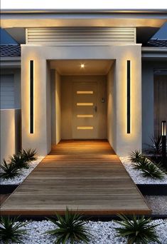 an entrance to a modern house with lights on the front door and wooden steps leading up to it